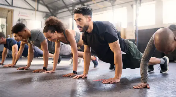 Gruppe trainiert Liegestütze im Fitnessstudio. Ein Mann mit Bart konzentriert sich auf sein ganzheitliches Training.